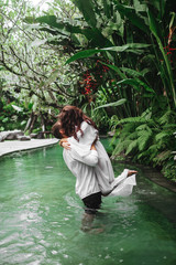 Happy couple kissing while relaxing in outdoor spa swimming pool surrounded with lush tropical greenery of Ubud, Bali. Luxury spa and wellness vacation retreat concept.