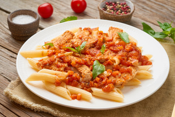 Wall Mural - Penne pasta, chicken or turkey fillet, tomato sauce with basil leaves on old rustic wooden background.