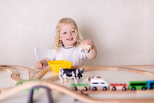 Little Cute Baby Boy (3 Years Old) Drinks Milk With Cookies And Plays In The Wooden Station Train Set On The Table.