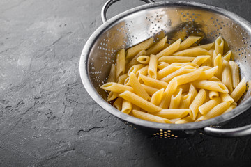 cooked Penne rigate pasta in stainless steel colander on Dark grey black slate background with copy space. top view