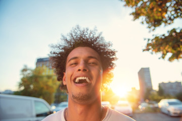 happy smiling urban hipster young man using smart phone. African american teenager holding mobile smartphone on sunset with lens flare