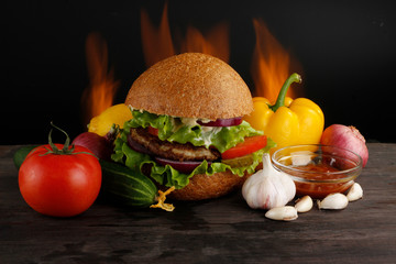 hambureger with vegetables on wooden table on fire background