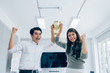 © Yingyaipumi - Businessman and Businesswomen team holding award trophy for show their victory.We are the champions! Successful business team with raised up hands in sunny modern workstation.