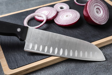 Board with sharp knife and cut onion on grey background