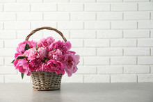 Wicker Basket With Fragrant Peonies On Table Against Brick Wall, Space For Text. Beautiful Spring Flowers