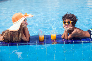 Wall Mural - Two kids girl and boy drink juice in the pool and have fun. Children and summer concept