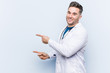 © Asier - Young handsome doctor man excited pointing with forefingers away.