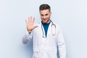 young handsome doctor man smiling cheerful showing number five with fingers.