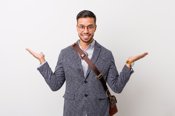 Young business filipino man against a white wall makes scale with arms, feels happy and confident.