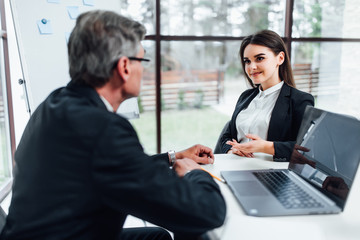 Wall Mural - Older boss listening young manager woman in office, they are working with notebook.