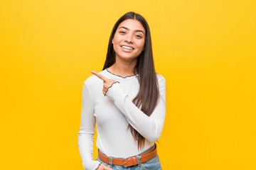 Wall Mural - Young pretty arab woman against a yellow background smiling and pointing aside, showing something at blank space.