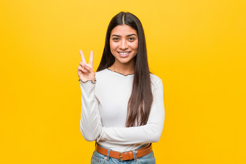 young pretty arab woman against a yellow background showing number two with fingers.