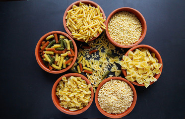 Flat lay of macaroni. Different kinds of spaghetti on the black background. Macaroni isolated on the black background. Black background in sunlight. Cuisine concept. 