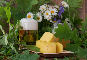 Two glasses of light beer with cheese a bouquet of daisies and oak on a wooden background. Celebration of a traditional holiday in Latvia Ligo in June