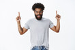 © Cookie Studio - You wanna see it. Portrait of enthusiastic attractive happy young african american masculine man with curly hair, tattoos and pierced nose raising hands up, pointing upwards and smiling
