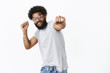 © Cookie Studio - Yo join me in dance competition. Portrait of happy enegized good-looking african american guy in glasses with ring and pierced nose smiling pulling fist towards camera while dancing, shaking hands