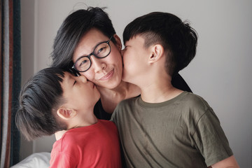 Two sons kissing their mother at home, Happy Asian family portrait