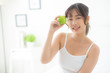 © NT_studio - Beautiful young asian woman holding and eating green apple fruit in the bedroom at home, lifestyle of nutrition girl healthy and care weight loss, health and wellness concept.