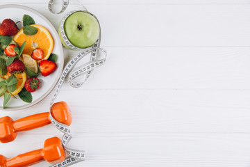 Diet plan, menu or program, tape measure, water, dumbbells and diet food of fresh fruits on white background, weight loss and detox concept, top view