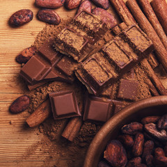 Chocolate pieses with cocoa powder and cocoa grains on wooden background