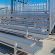 Square frame Raised tiered rows of benches with railings at a sports filed on a sunny day