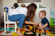 Side view of young mother sitting on child chair and soothing crying baby while playing with cars in children room at home