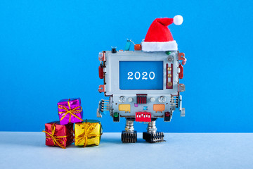 Merry Christmas Happy 2020 year greeting card. Robotic computer Santa Claus red hat and gift boxes and congratulation message 2020 on blue screen. Modern style winter holidays poster for IT