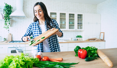 Wall Mural - Beautiful young woman is preparing vegetable salad in the kitchen. Healthy Food. Vegan Salad. Diet. Dieting Concept. Healthy Lifestyle. Cooking At Home. Prepare Food. Cutting ingredients on table