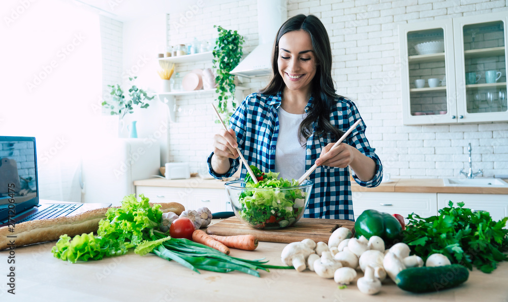 Beautiful young woman is preparing vegetable salad in the kitchen. Healthy Food. Vegan Salad. Diet. Dieting Concept. Healthy Lifestyle. Cooking At Home. Prepare Food. Cutting ingredients on table - obrazy, fototapety, plakaty 