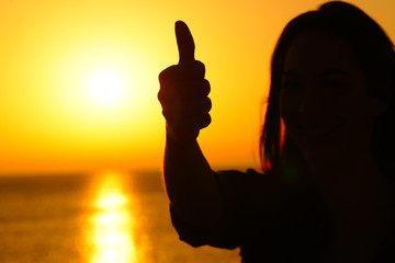 Woman silhouette gesturing thumb up at sunset
