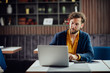 © chika_milan - Young serious bearded businessman in smart casual clothes sitting in cafe and typing on laptop.