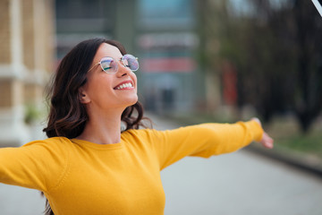 Young woman with toothy smile and eyes closed spreading arms wide open, in the city.