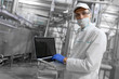 © Ivan Traimak - Portrait of man in a white robe and a cap standing in production department of dairy factory with grey tablet