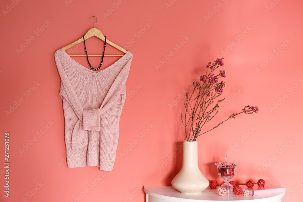 Table with decor and female clothes hanging on color wall in room