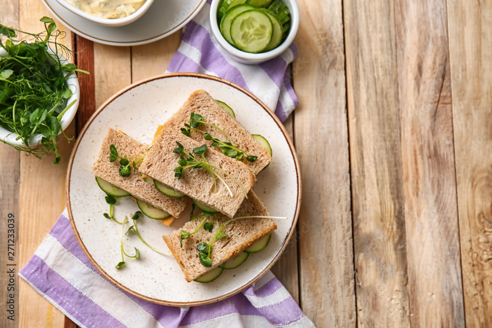 Plate with tasty cucumber sandwiches on wooden table