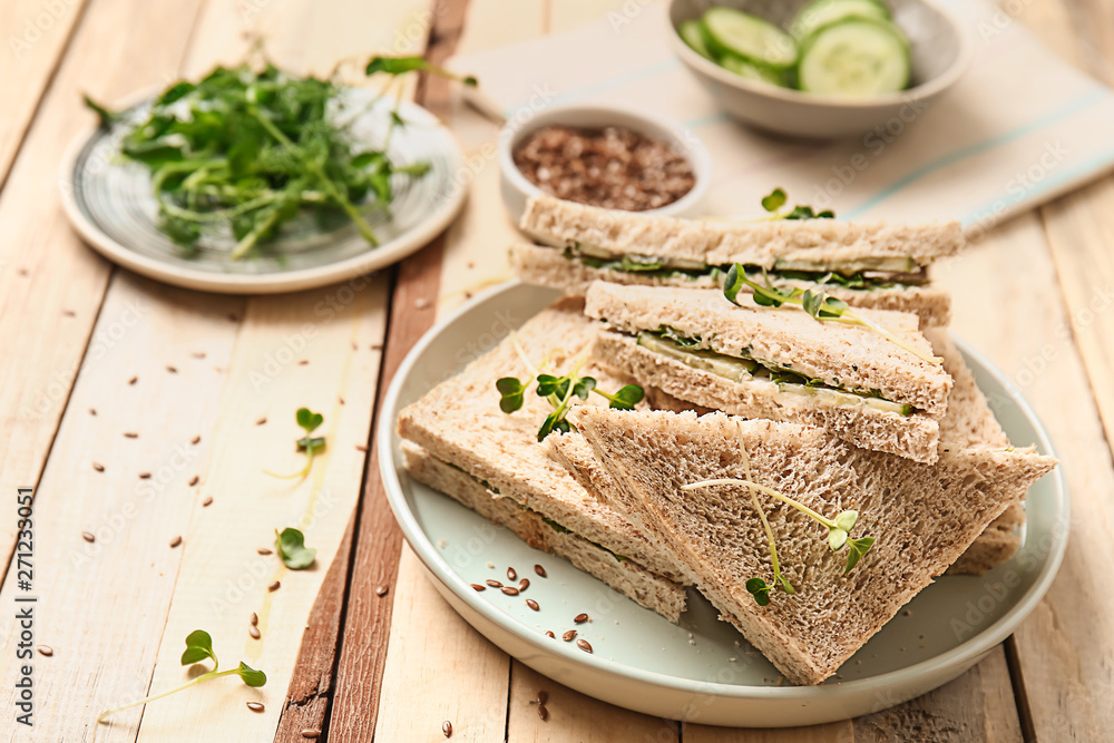 Plate with tasty cucumber sandwiches on wooden table
