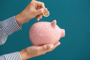 Woman putting coin into piggy bank on color background. Money savings concept