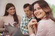 © mad_production - Close up of a lovely happy young female student smiling to the camera over her shoulder, enjoying studying with her college friends