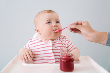 Wall Mural - Cute little baby eating tasty food on grey background