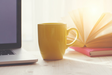 Wall Mural - open laptop, coffee cup and open books on wooden table, morning sunshine