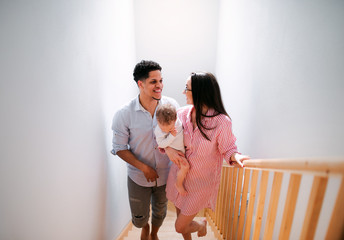 Wall Mural - Portrait of young family with small toddler son indoors at home, walking up the stairs.