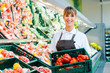 Verkäuferin im Supermarkt zeigt frisches Gemüse
