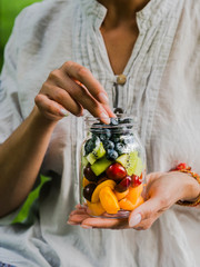 A glass jar with a salad of fruits and berries in the hands of a woman. Seasonal healthy healthy vegetarian food for a picnic