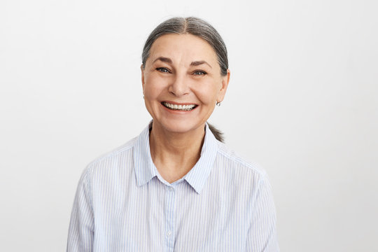 Joy, happiness, aging, old people and positive vibrations concept. Picture of happy elegant senior 65 year old female in good mood wearing blue shirt looking at camera with broad cheerful smile