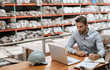 © mavoimages - Warehouse manager checking stock with a laptop and writing notes