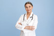 © shurkin_son - People, aging, occupation and profession concept. Confident attractive mature sixty year old female pediatrician wearing white medical overall and stethoscope posing at blue wall with arms crossed