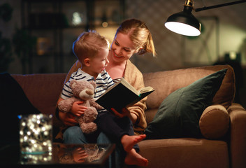 Wall Mural - Family before going to bed mother reads to her child son book near a lamp in the evening