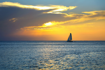 Wall Mural - Colorful seascape image with shiny sea and sailboat over cloudy sky and sun during sunset in Cozumel, Mexico