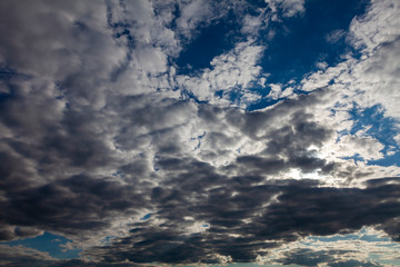 Torn white clouds lit by the rays of the setting sun against a deep blue sky