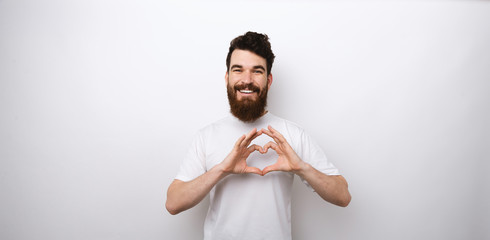 Portrait of smiling bearded man making heart symbol over white background